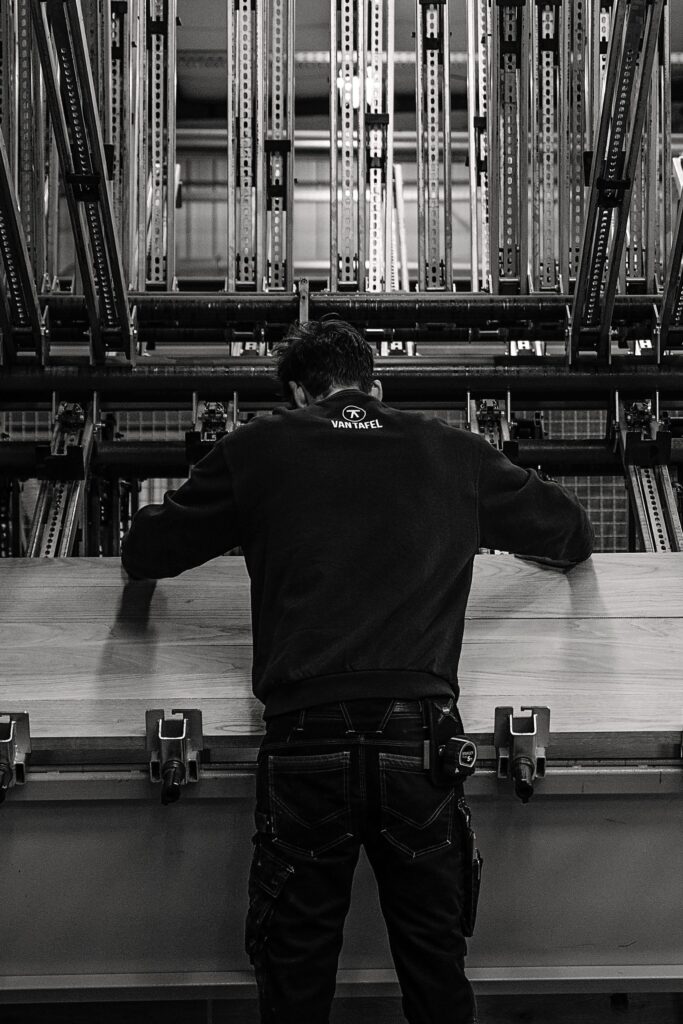 achterkant van iemand die aan de lijmmachine staat in de werkplaats van Van Tafel